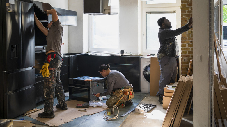 Three people doing renovation work on a kitchen