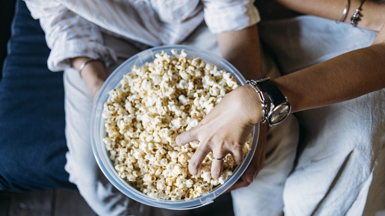 hands grab buttered popcorn from a bowl