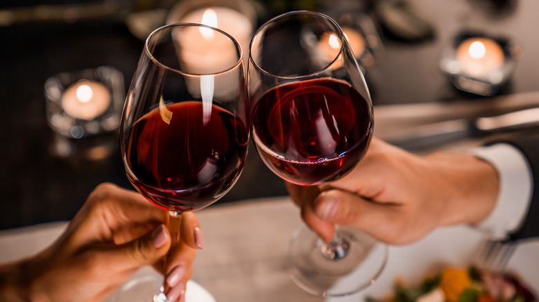 two people clinking bases of wine glasses