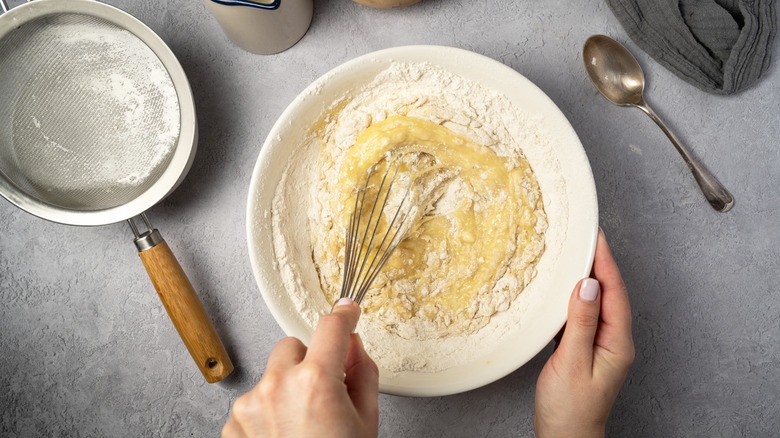 Overhead view of hand whisking dry and wet ingredients together.