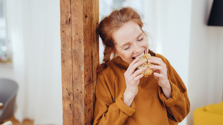 Woman bites into sandwich while standingin doorway.