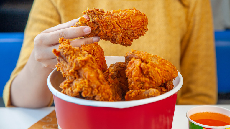 woman holds piece of fried chicken from bucket