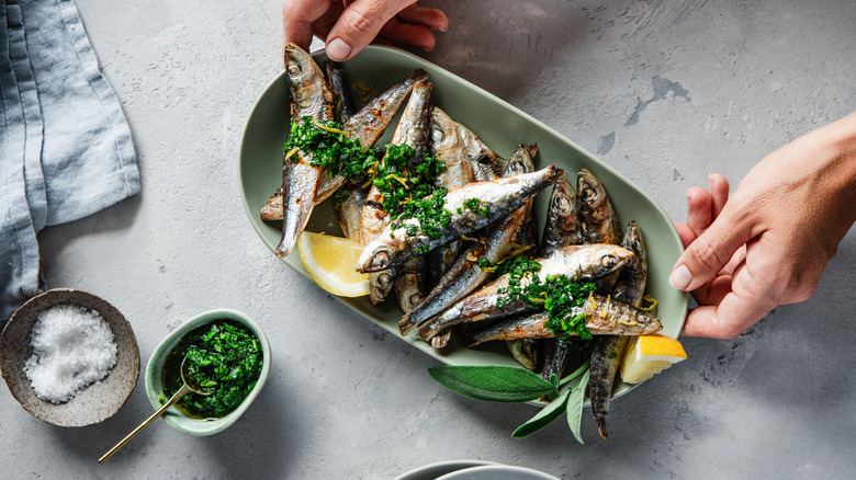 Someone placing down a plate of freshly grilled sardines