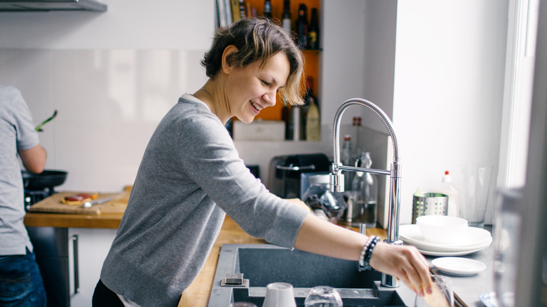 Smiling woman standing at kitchen sink.
