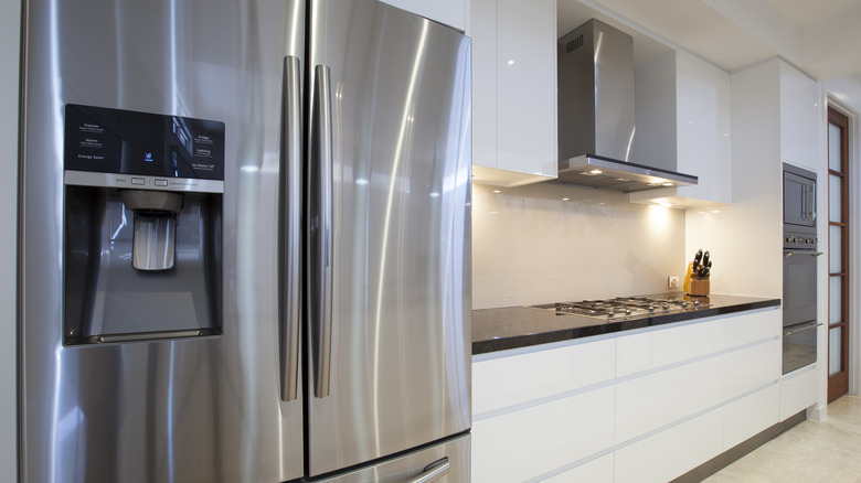 A shot of a modern kitchen with a stainless steel fridge, stovetop vent hood, and oven