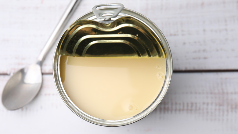 A half-open can of condensed milk on a white wooden table