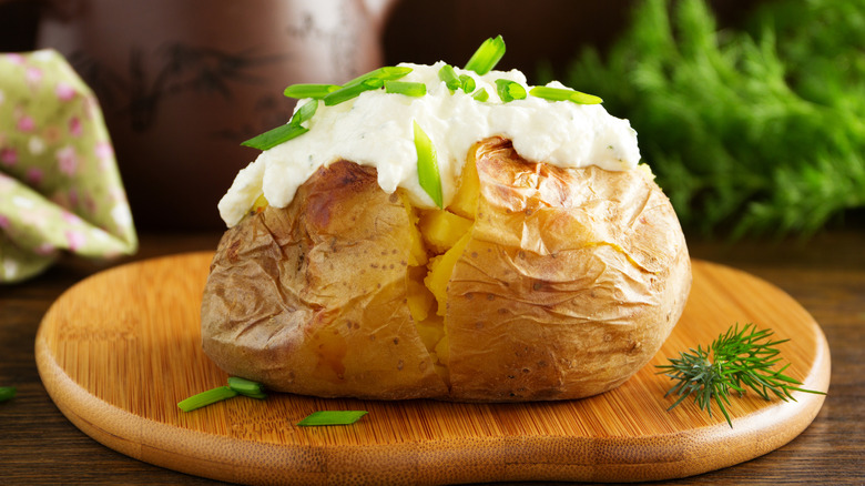 classic baked potato with sour cream and green onion on small wooden board.