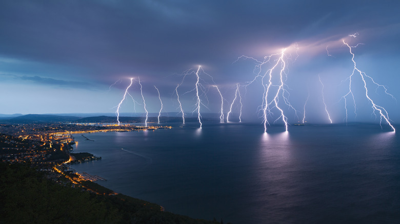 A landscape shot of a coast town during a thunderstorm, with several lightning strikes out in the ocean