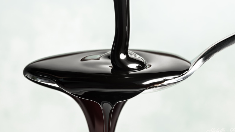 Dark molasses pouring into a spoon.
