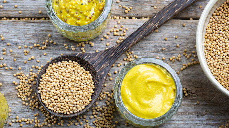 Different types of mustard and seeds on a rustic wooden board