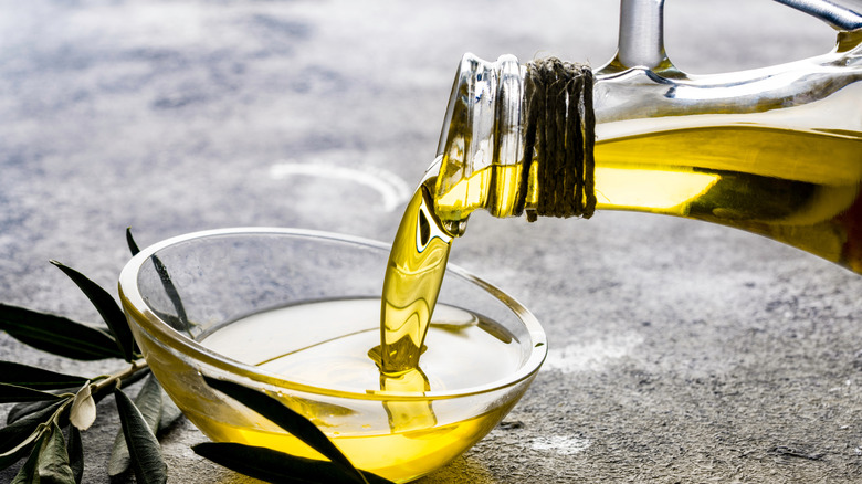 Olive oil being poured from a bottle into a glass bowl