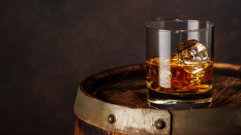 glass of bourbon sits atop wooden cask