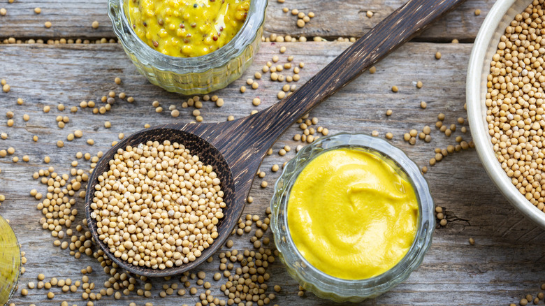 Different types of mustard and mustard seeds on a wooden surface