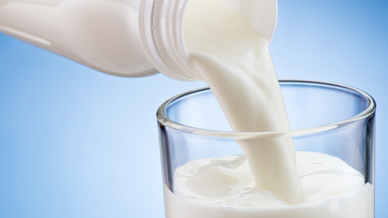 Close-up of milk pouring into a glass from plastic bottle on a blue background