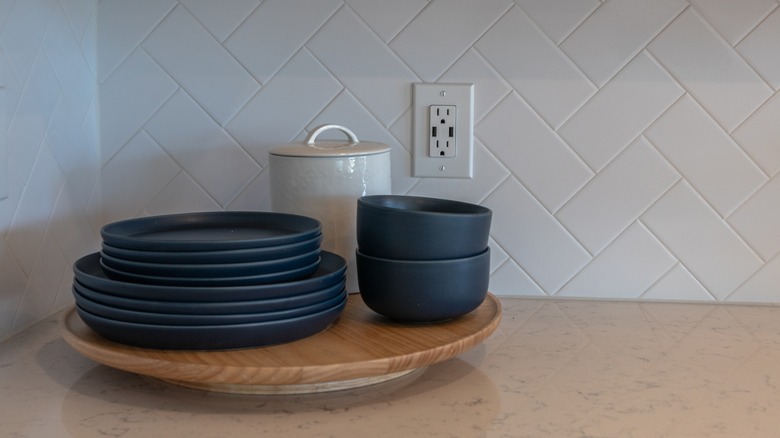A Lazy Susan with black plates and bowls on it on top of a counter next to an electrical outlet
