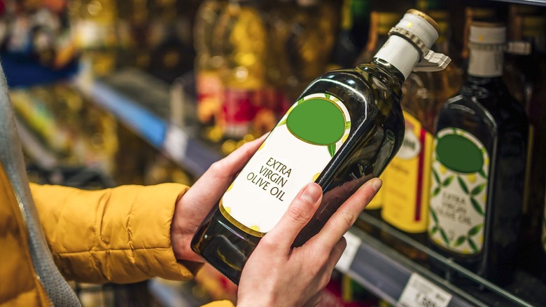 Person holding extra-virgin olive oil in grocery aisle
