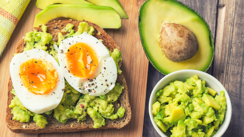 Bowl of guacamole with halved avocado on dark background