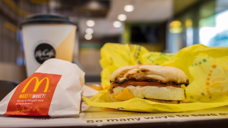 an eggmcmuffin and side of hash browns on a mcdonald's table, with a coffee in the background