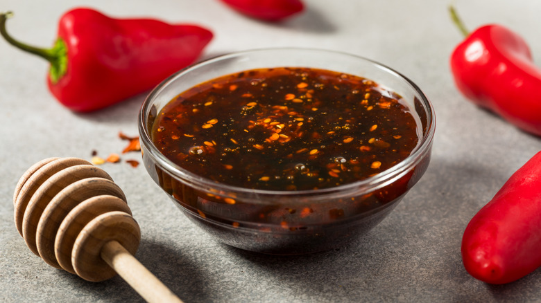 A close-up of a bowl of hot honey with peppers surrounding it and a honey wand to the left