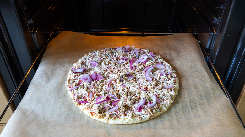 A frozen pizza ready to go into an oven on top of wax paper