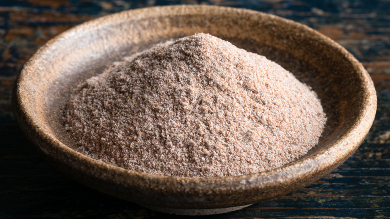 A close-up of a small wooden bowl of teff flour on a wooden background