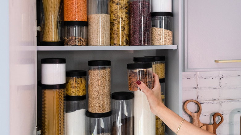Hand reaching into a pantry with two shelves of different sized glass jars