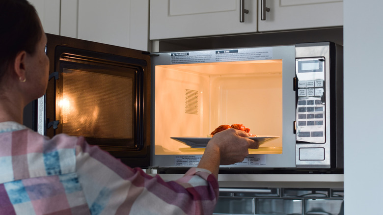 Woman placing plate of food into a microwave oven
