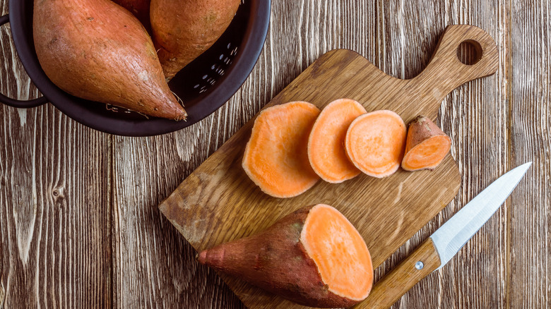 Whole and sliced yams on a cutting board with a knife.