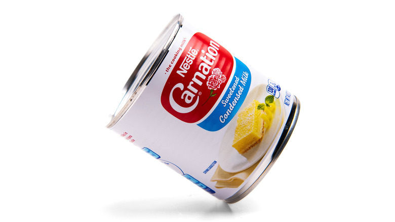 Tilted can of Nestle Carnation sweetened condensed milk on white background.