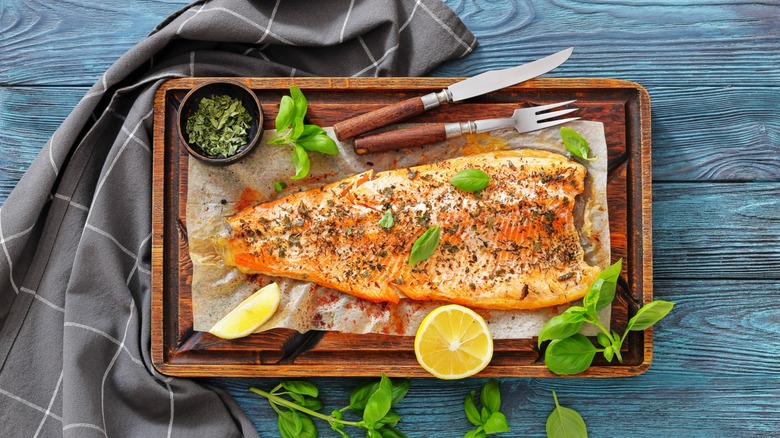 whole salmon filet on board with utensils and herbs