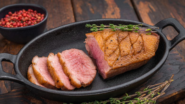 Seared duck breast sliced in cast-iron skillet with thyme