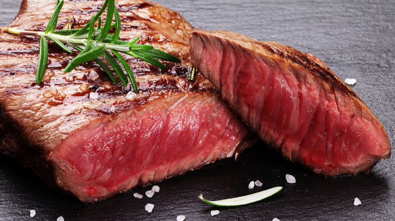 Grilled beef steak with rosemary, salt and pepper on a black stone plate