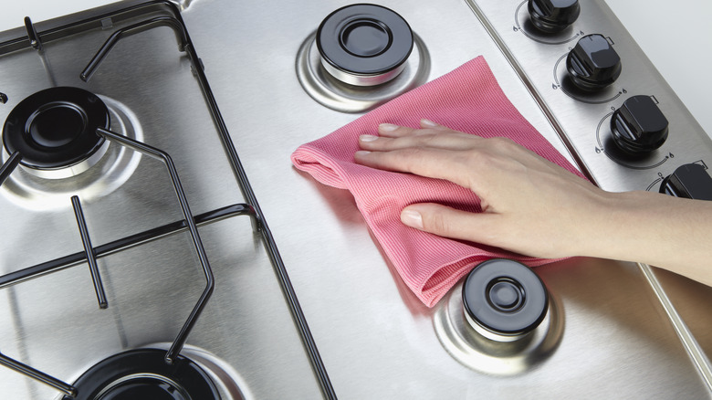 hand wiping a stainless steel stovetop with a pink microfiber cloth