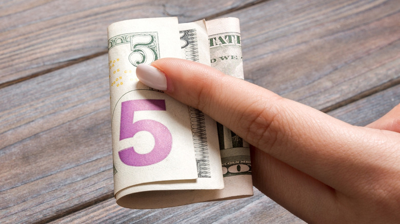 Someone holding a 5 dollar bill between their fingers
