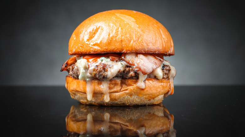 Wagyu burger with cheese on dark backdrop.