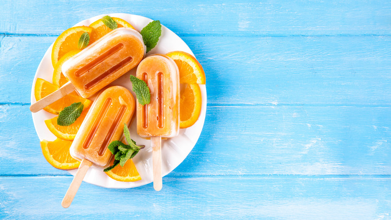 Plate of orange popsicles on a white plate with orange slices, blue background