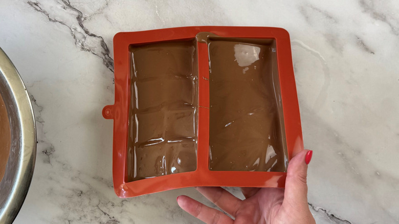 Hand tilting candy bar mold with melted chocolate inside