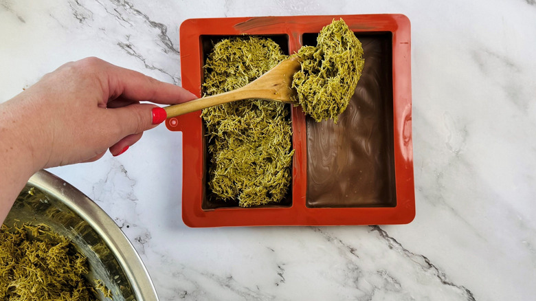 Wooden spoon scooping pistachio kataifi filling into chocolate bar molds