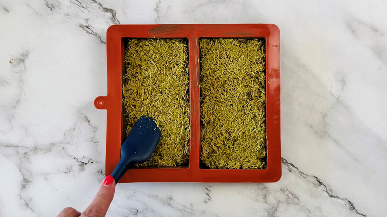Rubber spatula pressing kataifi filling into chocolate bar molds
