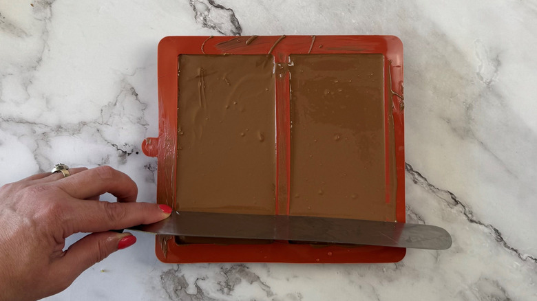 Offset spatula smoothing chocolate surface on candy bar molds