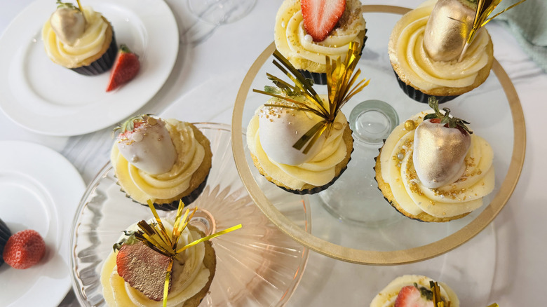 yellow cupcakes with white frosting, strawberries, and other decorations