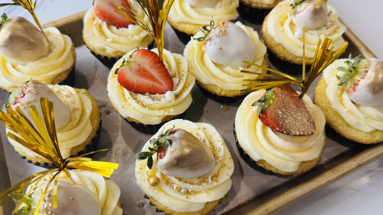 yellow cupcakes with white frosting and assorted decorations in a pan