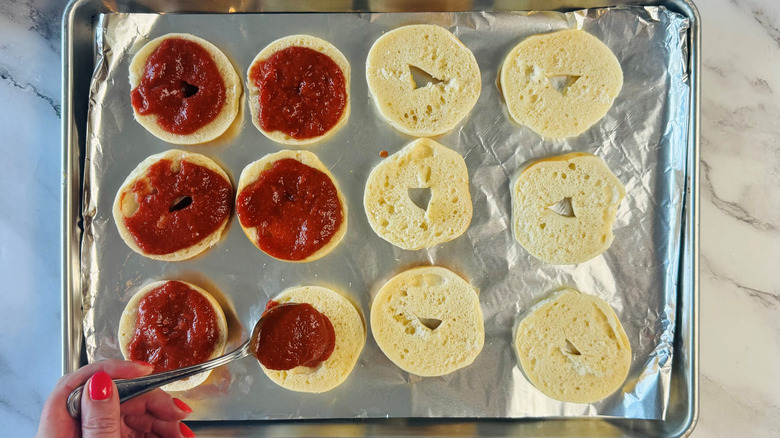 person using a spoon to top bagel halves with sauce