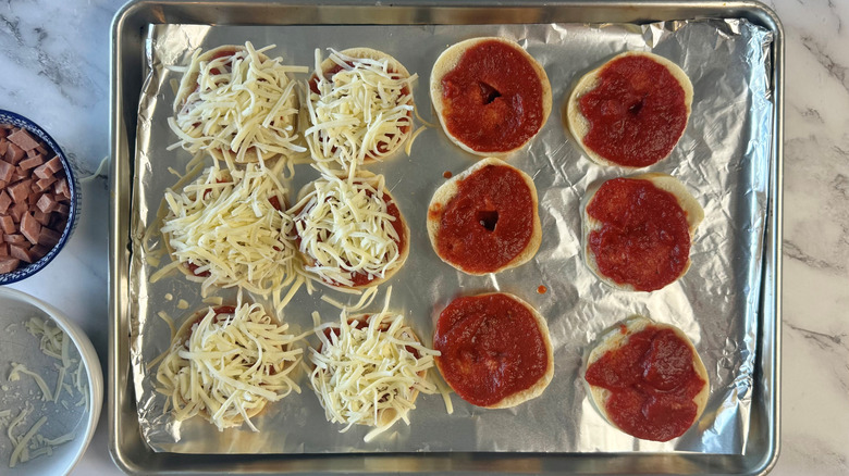 bagel halves topped with tomato sauce or cheese on lined baking sheet
