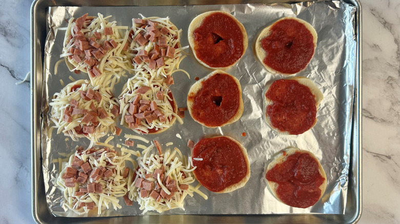 bagel halves topped with tomato sauce, pepperoni, and cheese on lined baking sheet