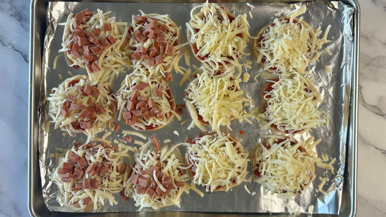 bagel halves loaded with cheese and toppings on lined baking sheet