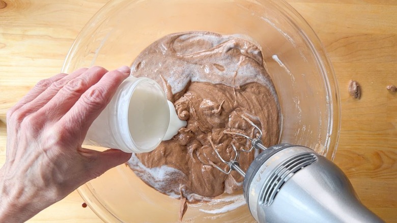 Adding buttermilk to traditional German chocolate cake batter in glass bowl
