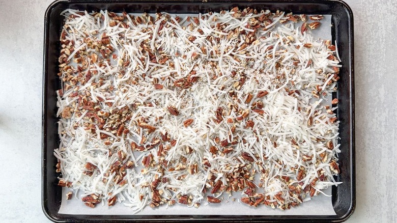 Shredded coconut and chopped pecans on parchment-lined baking sheet