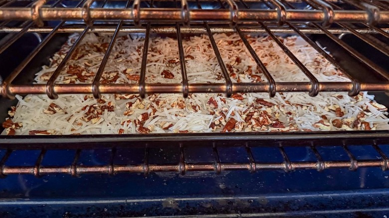 Shredded coconut and chopped pecans toasting on baking sheet in oven