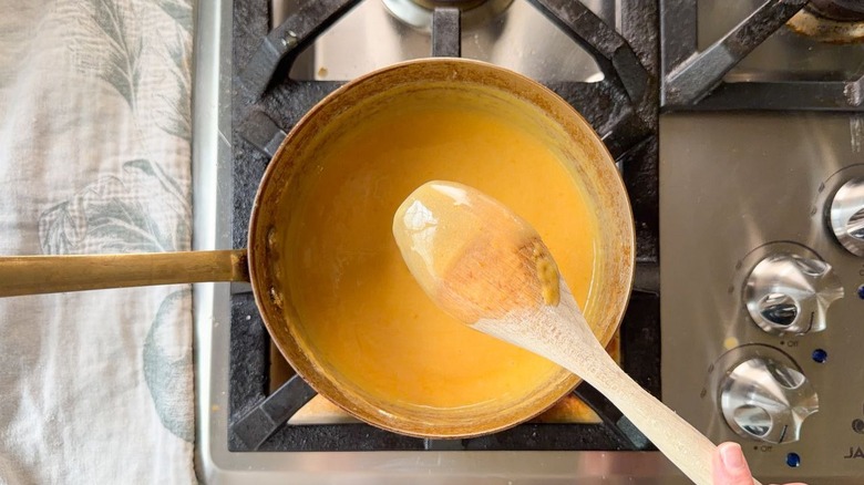 Cooked custard coating the back of a wooden spoon over a saucepan on stovetop